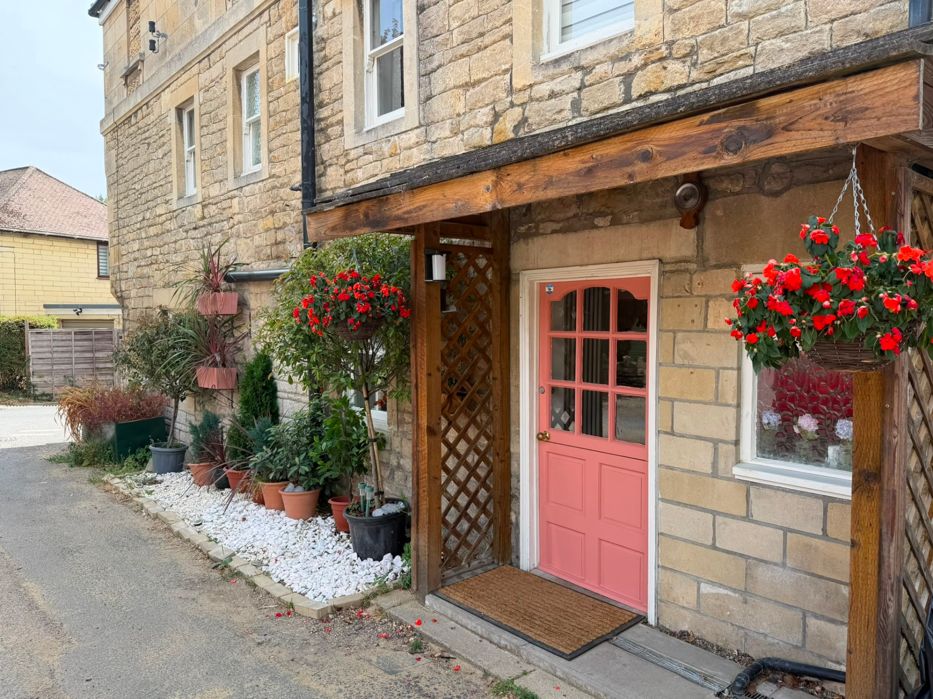 Bath stone frontage with a coral front door and hanging flower baskets