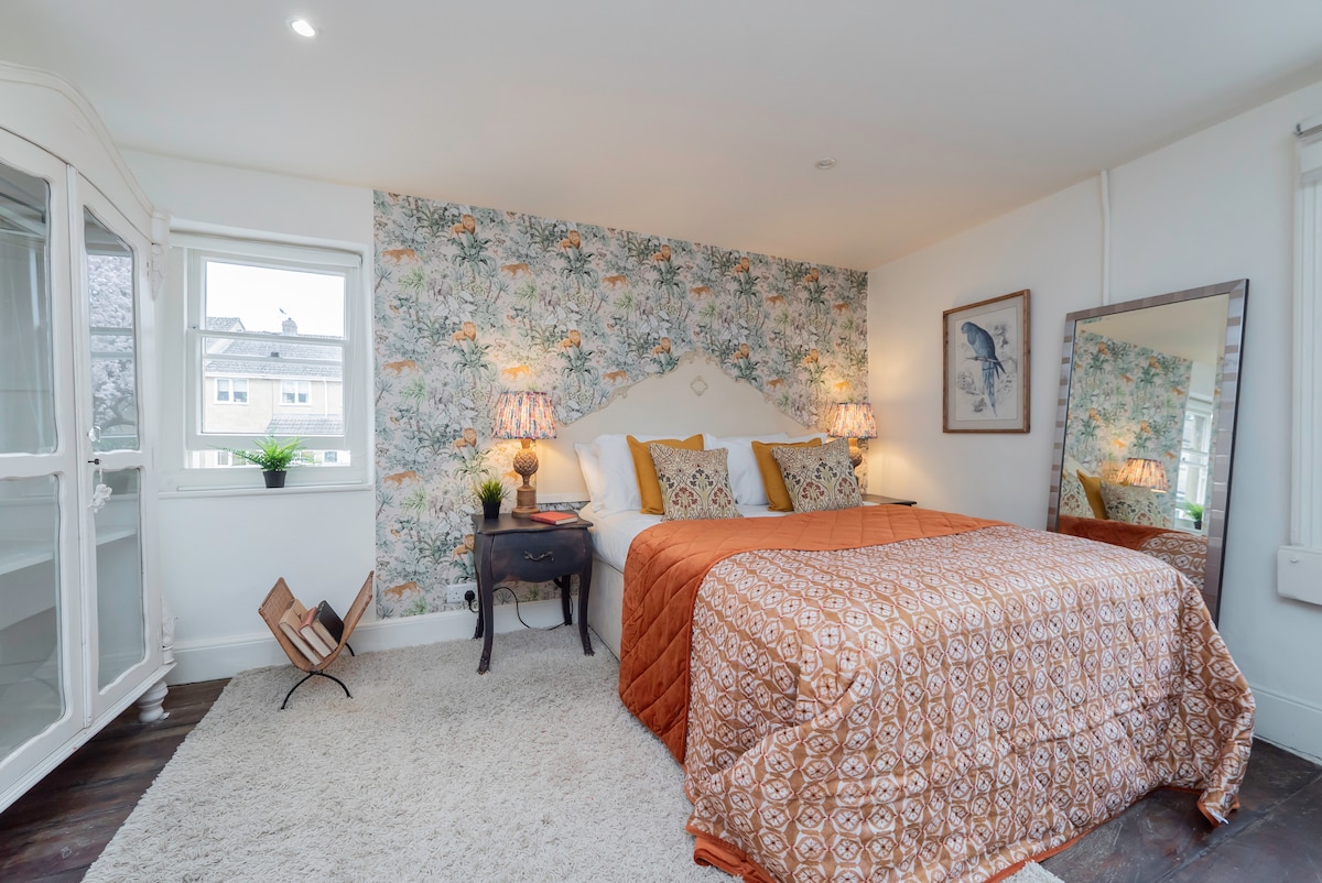 Bedroom with jungle print wallpaper, mustard cushions and a terracotta throw