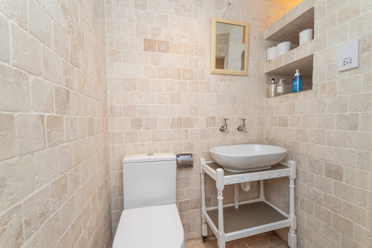 Travertine tiled cloakroom with a basin on a white stand