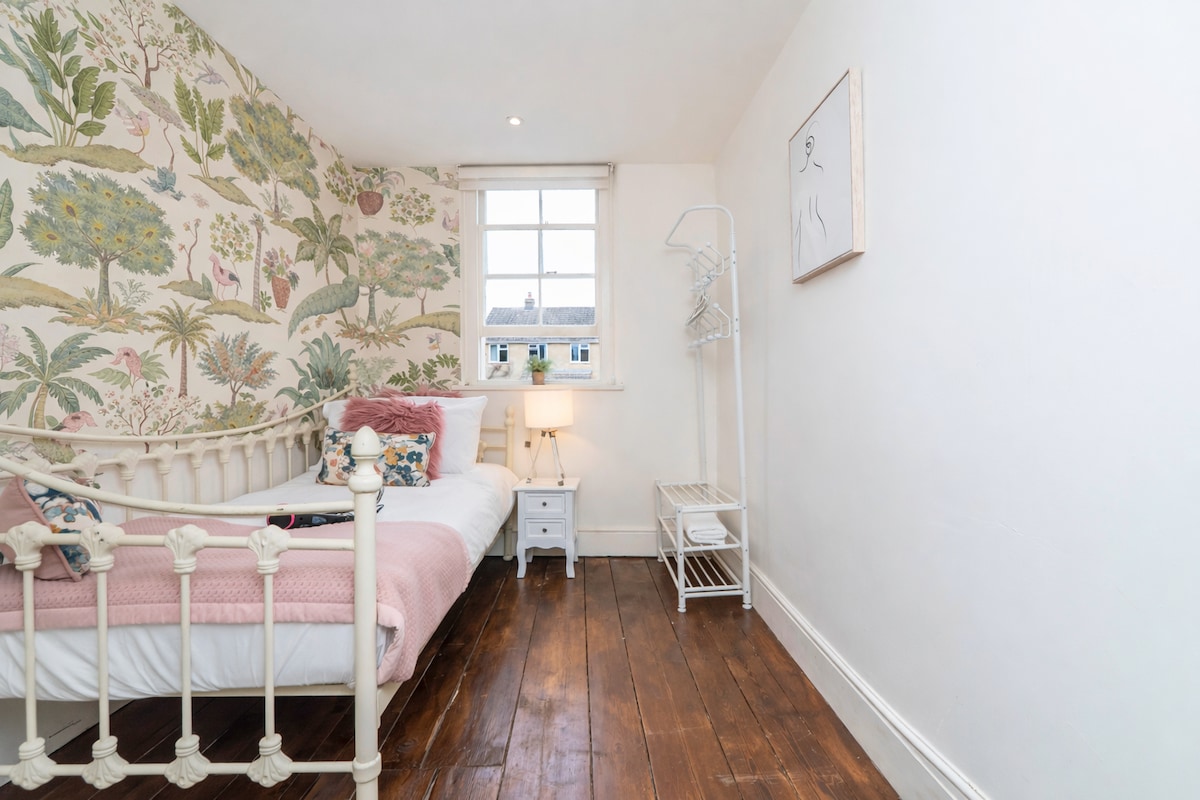 Single bedroom with botanical wallpaper and a cast-iron bed