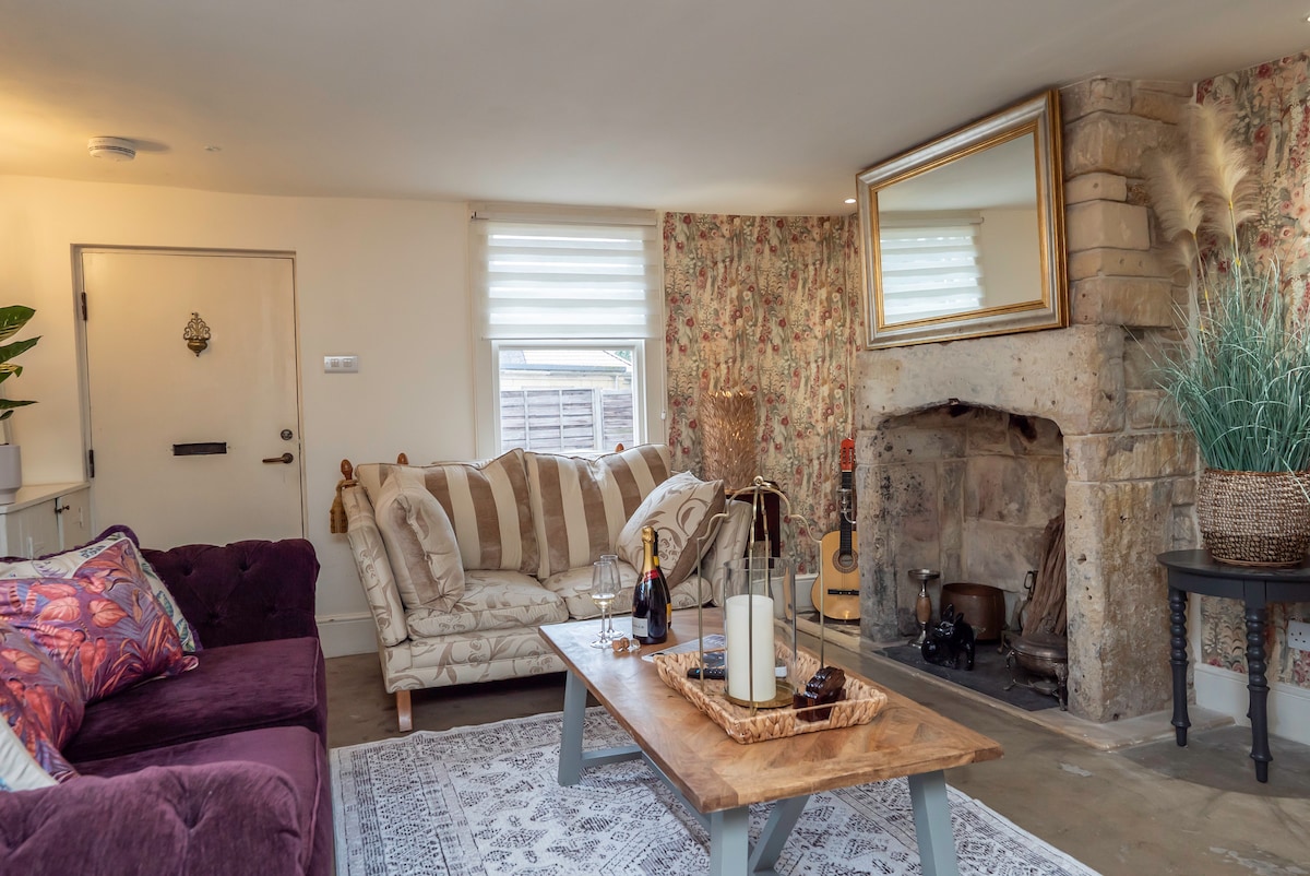 Snug with a stone inglenook fireplace, velvet sofa and floral wallpaper