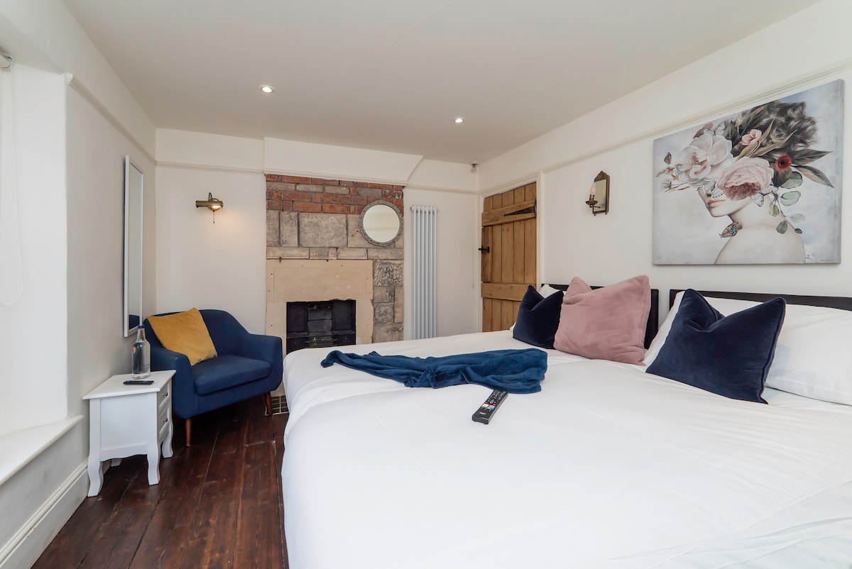 Cottage bedroom with an exposed brick fireplace and blue armchair