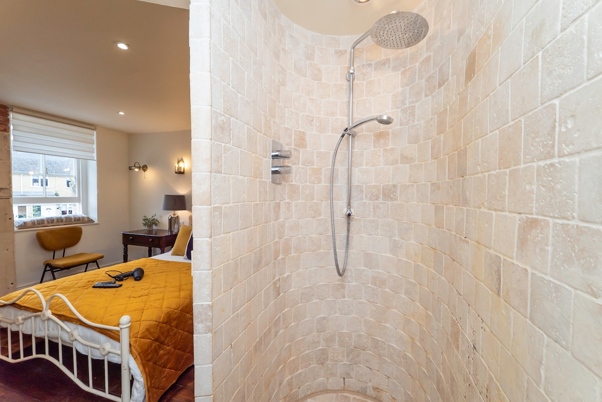 Curved travertine walk-in shower beside a cottage bedroom