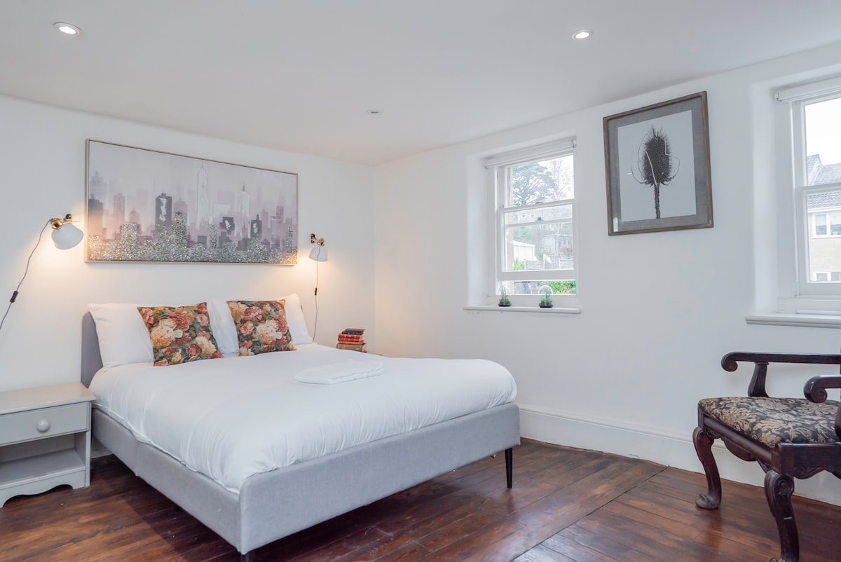 Main house bedroom with a king bed, floral cushions and dark wood floors